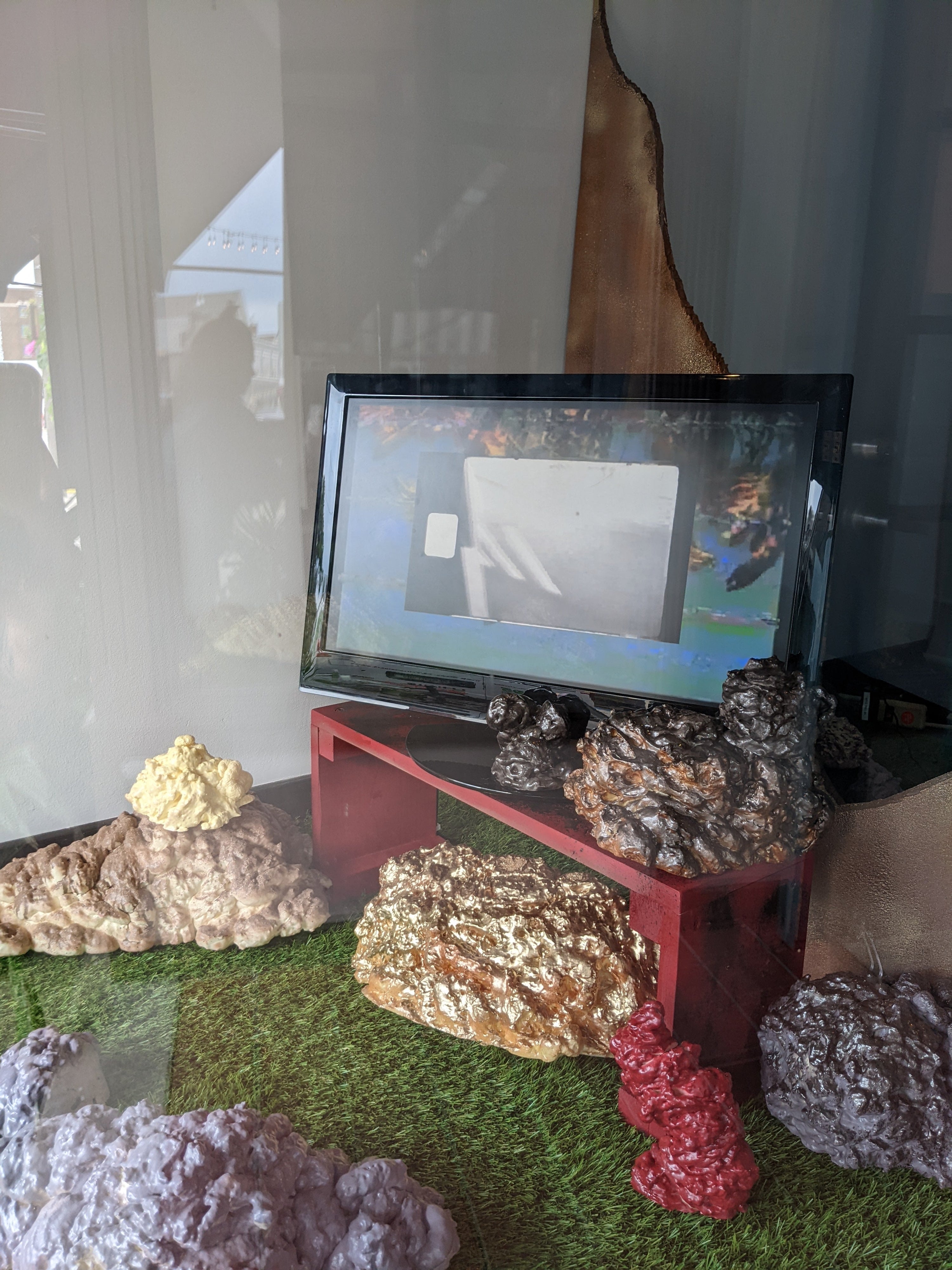 A tv with video playing surrounded by fake grass and faux stones