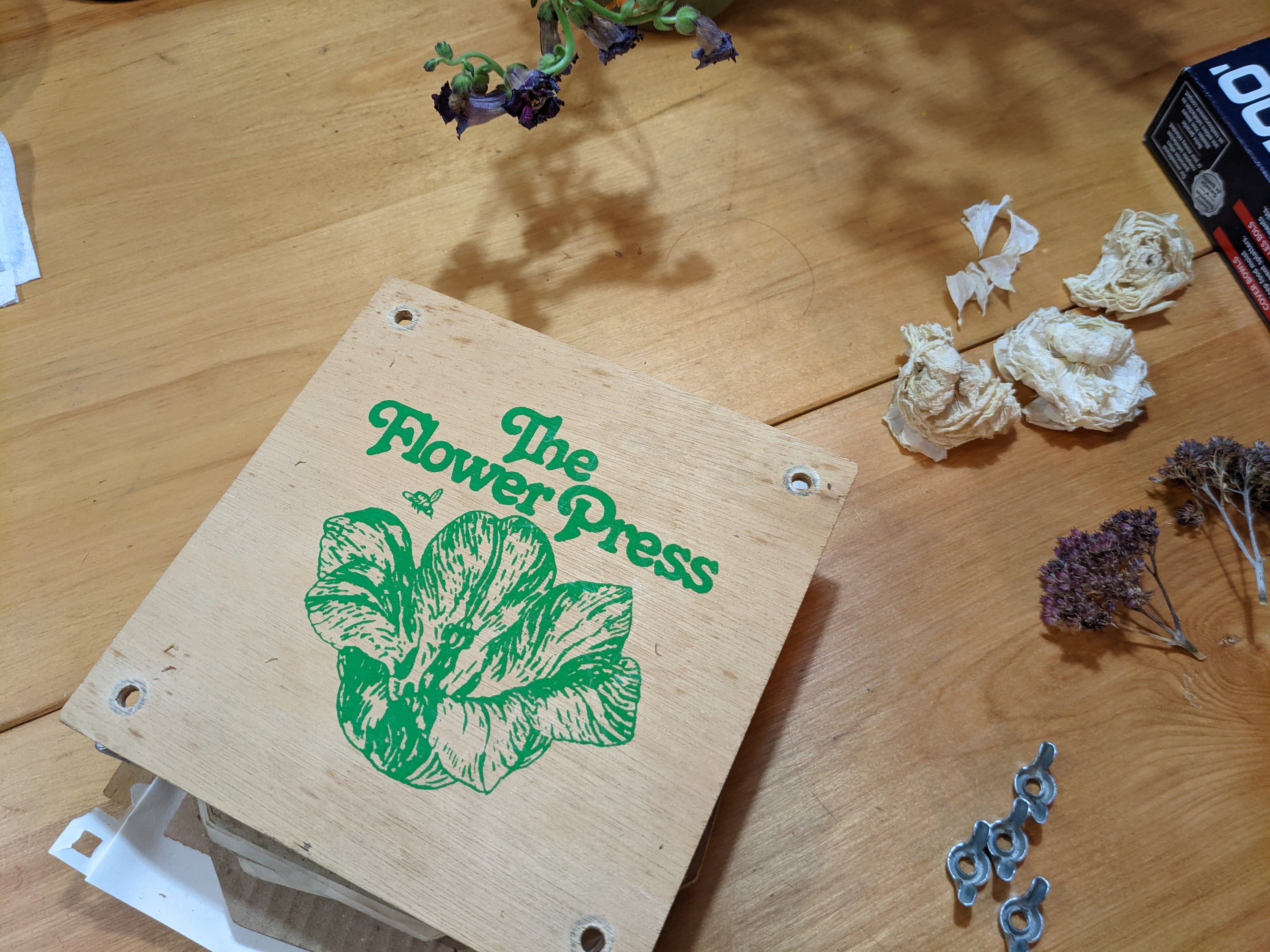 A flower press on a wooden table surrounded by petals and flowers