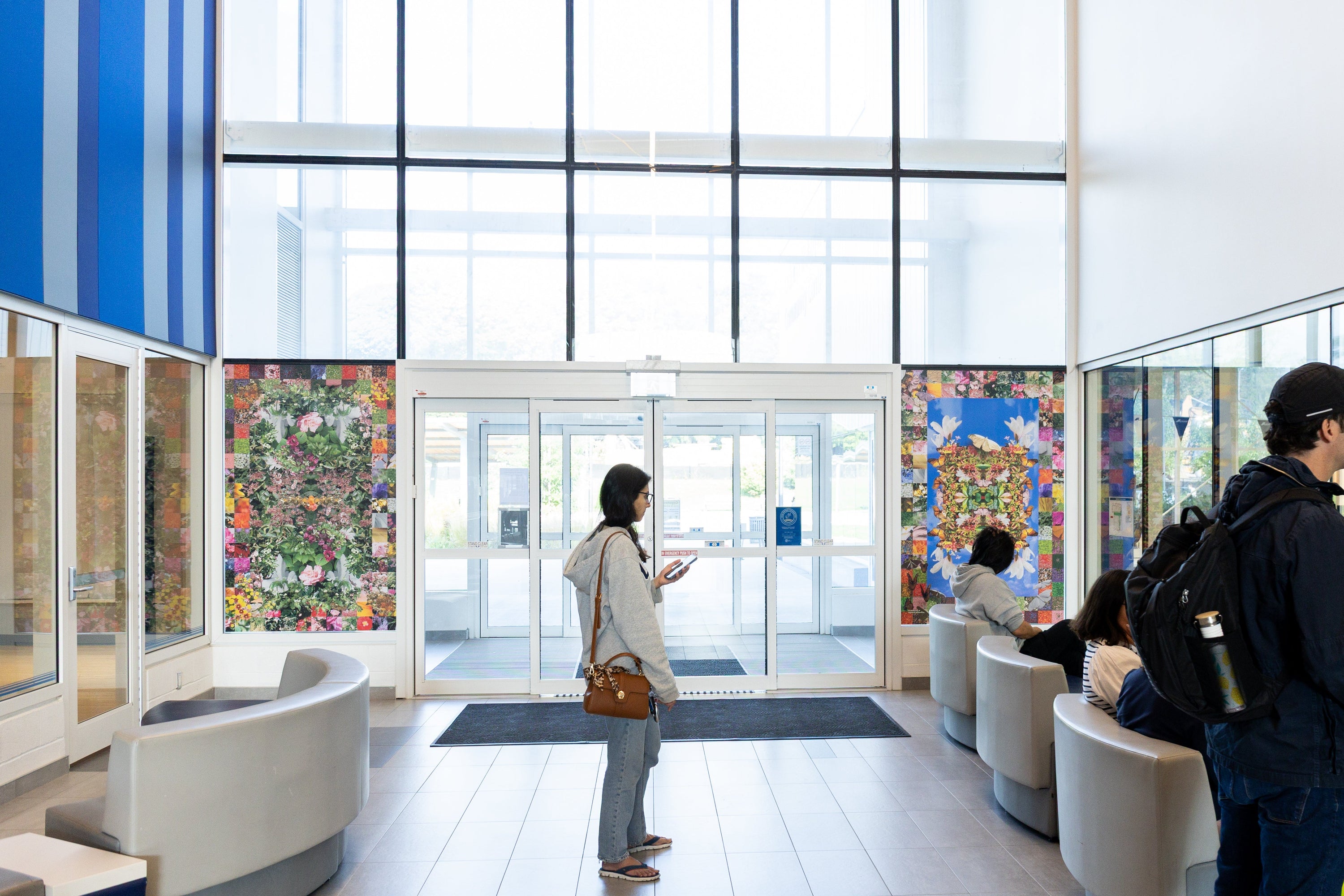 A building with people standing looking at the pool on the right side of the image. Two pieces of artwork installed beside the sliding doors in the background.